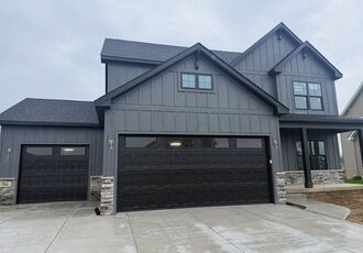 Farmhouse-style home with new black garage doors